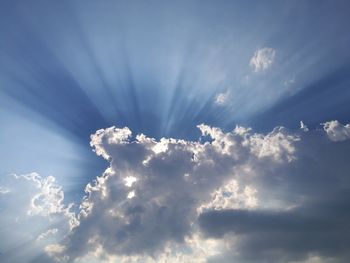 Low angle view of sunlight streaming through clouds