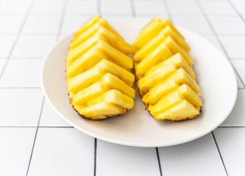 Two beautifully sliced pineapple halves on a white plate, placed on a tiled surface. flat lay