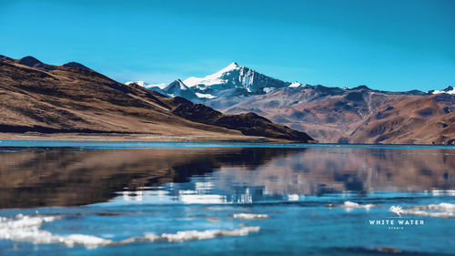 Scenic view of lake and snowcapped mountains against blue sky