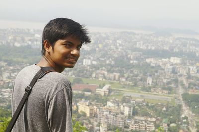 Rear view portrait of smiling young man standing against cityscape