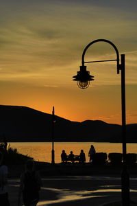 Silhouette people on street against orange sky