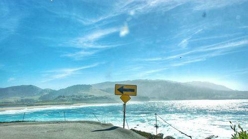 Sign on road by sea against sky