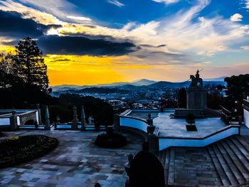 Statue in city against sky at sunset