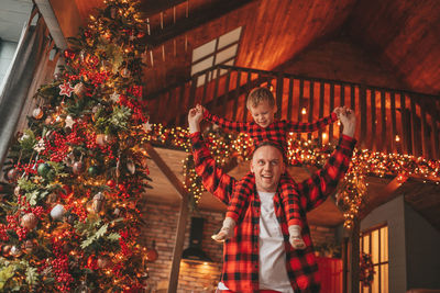 Candid authentic happy dad and son in red plaid pajamas fooling around at wood lodge xmas decorated