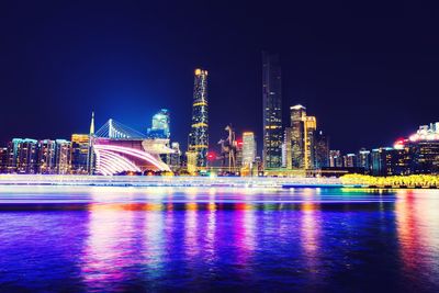 Illuminated city by river against sky at night