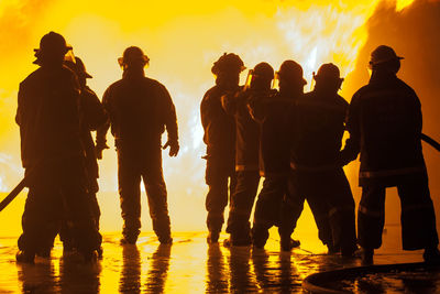 Silhouette firefighters spraying water on fire at night