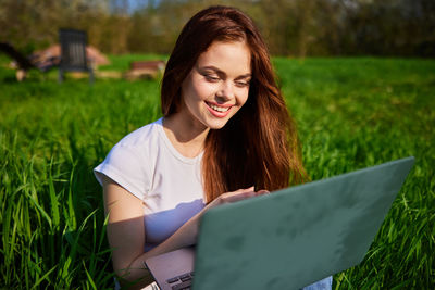 Young woman using laptop while sitting on field