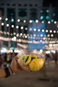 Close-up of hand holding salad in bowl at night