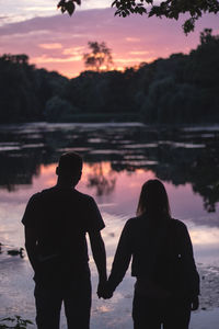 Rear view of couple standing at lakeshore during sunset