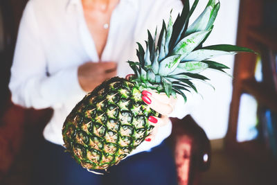 Midsection of woman holding pineapple at home