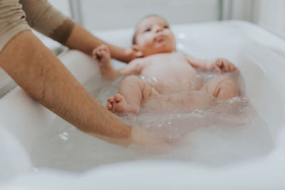 Close-up of father holding baby girl in bathtub at bathroom
