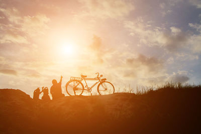 Silhouette people by bicycle against sky during sunset