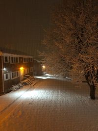 Snow covered road by buildings at night