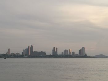 Sea by cityscape against sky during sunset