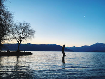 Silhouette sculpture in lake against sky during sunset