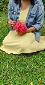 Midsection of woman holding red flowering plants on field