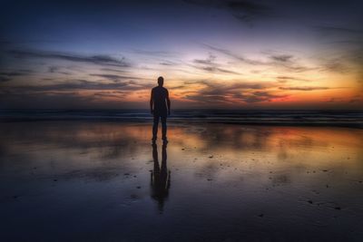 Silhouette man standing with reflection on shore at beach against sky