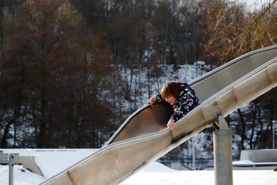 Boy playing on slide over snow covered playground