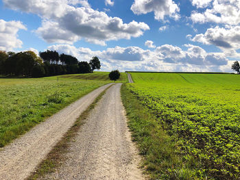 Empty road amidst field against sky
