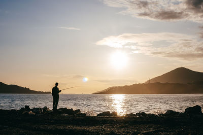 Silhouette man standing on beach against sky during sunset