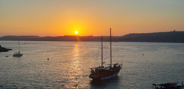 Sailboats moored on sea against sky during sunset