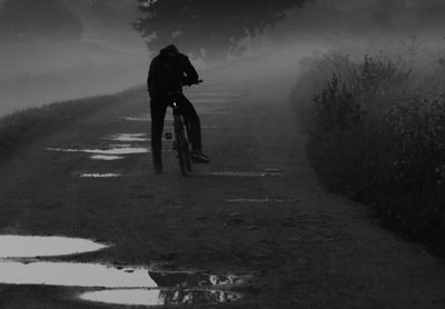 Man with bicycle on dirt road during foggy weather