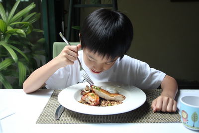 Boy having food in plate on table at home