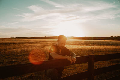 Man standing by railing at farm during sunset