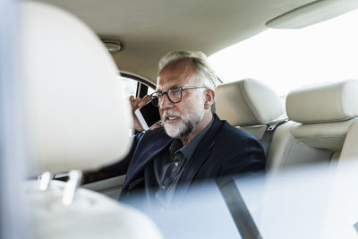 Mature businessman sitting on backseat in car, talking on the phone