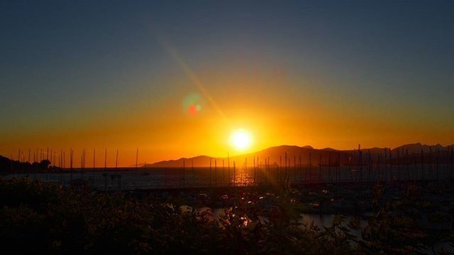 sunset, sun, orange color, scenics, water, beauty in nature, tranquil scene, tranquility, sea, nature, idyllic, sunlight, mountain, clear sky, sky, copy space, beach, silhouette, nautical vessel, sunbeam