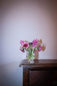 Pink flowers in a vase on table against wall