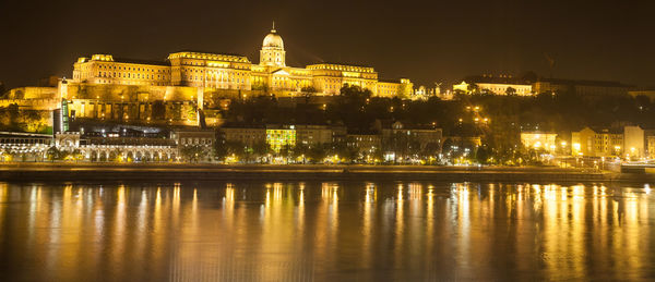 Illuminated buda castle by danube river against sky at night