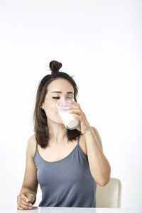 Portrait of a young woman drinking glass against white background