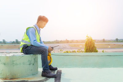 Side view of man sitting against sky