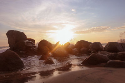 Rocks on beach against sky during sunset