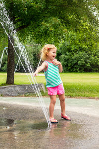 Little smiling child playing with water at splash pad in the local public park on hot summer day. 