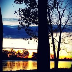 Silhouette trees by lake against sky during sunset