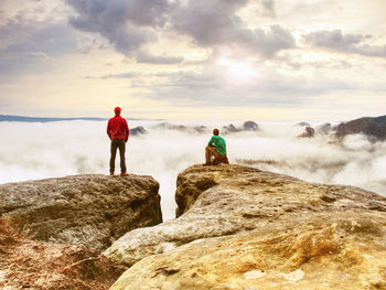 Silhouettes of photographers. hiker guide and photographer kneeing at tripod on cliff watch daybreak