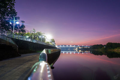 Illuminated city by river against sky at night