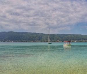 Boats sailing in sea against cloudy sky