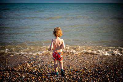 Rear view of shirtless boy walking at beach