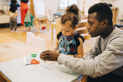 Mid adult male teacher playing with girl at table in child care classroom