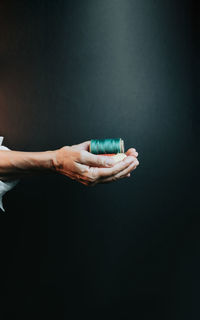 Cropped hand of woman holding electronic cigarette against black background