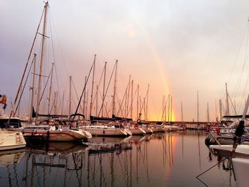 Sailboat sailing in harbor against rainbow in sky during sunset