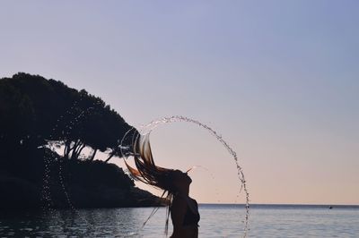 Silhouette woman tossing hair in sea against clear sky during sunset