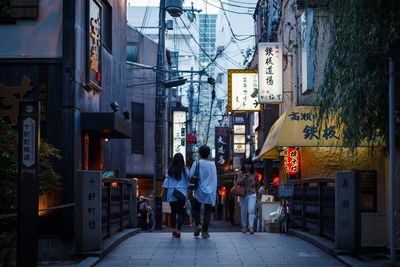 Rear view of people walking on street amidst buildings in city