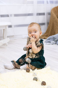 Adorable little baby girl in beautiful green dress is playing with christmas lights.