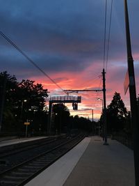 Railroad tracks by silhouette trees against sky during sunset