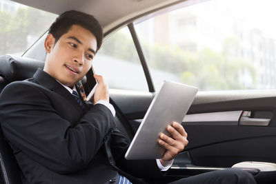 Businessman talking on phone while using digital tablet in car