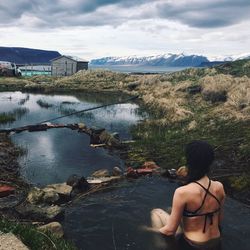 Rear view of woman sitting on riverbank against sky